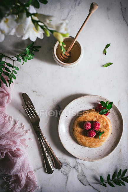 Delicioso panqueque rematado con frambuesas frescas y hojas de menta en plato blanco sobre mesa de mármol - foto de stock