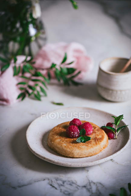 Tasty pancake topped with fresh raspberries and mint leaves on white plate on marble tabletop — Stock Photo