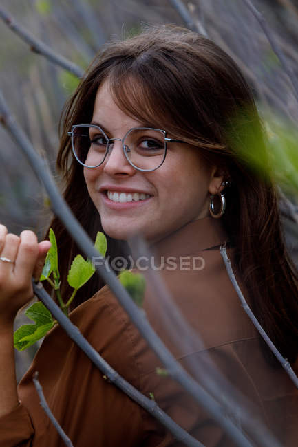 Vista lateral da bela mulher em pé na frente de arbustos olhando para a câmera — Fotografia de Stock