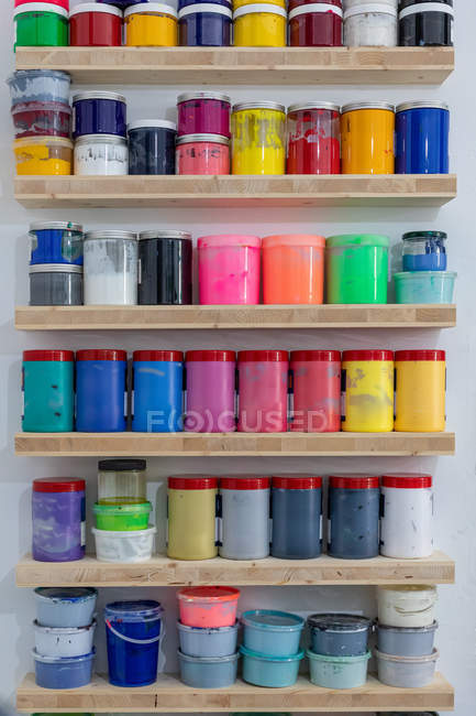 Shelves with colorful tins of paint of different shape size and colour at workplace — Stock Photo