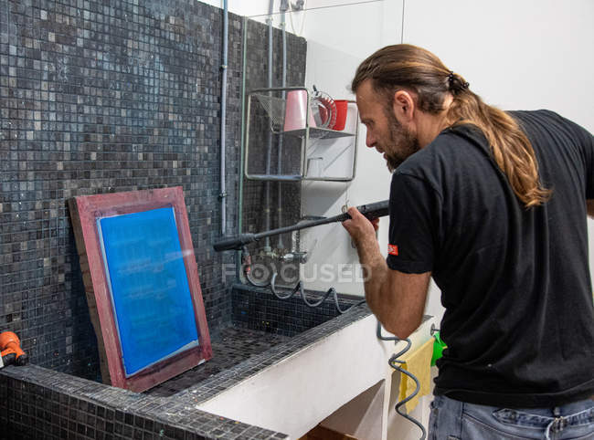 Artista maschile focalizzato con capelli lunghi che prepara serigrafia blu per serigrafia in officina — Foto stock