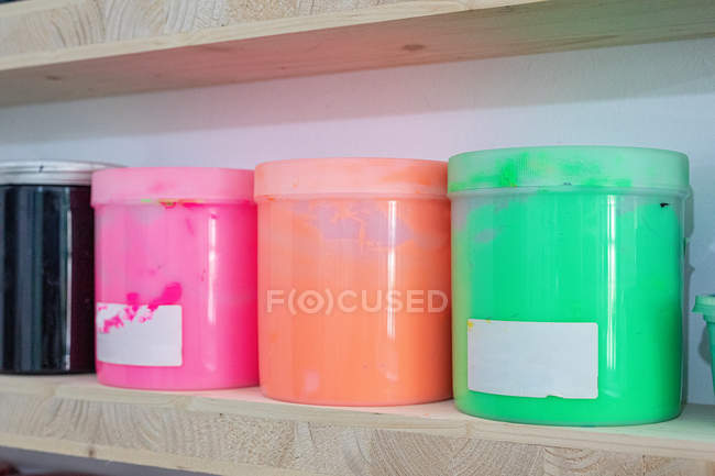 Regale mit bunten Farbdosen unterschiedlicher Form und Farbe am Arbeitsplatz — Stockfoto
