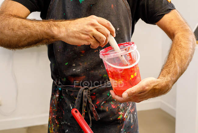 Hombre cultivador concentrado que lleva delantal sucio mezclando varias pinturas para serigrafía en taller. - foto de stock