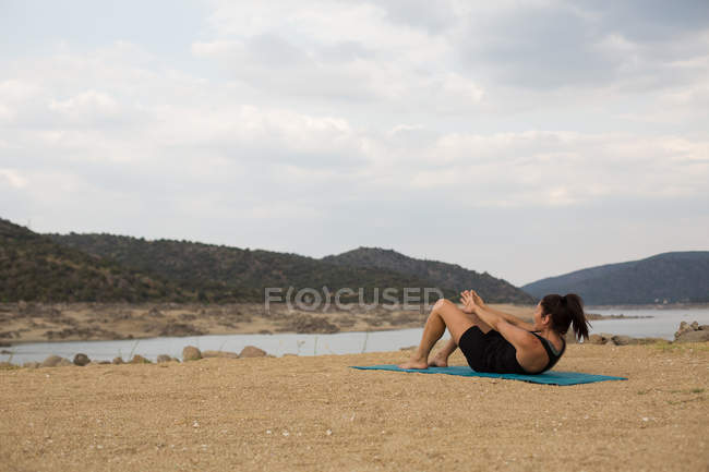Femme faisant du yoga en plein air par temps nuageux sur la plage du barrage — Photo de stock