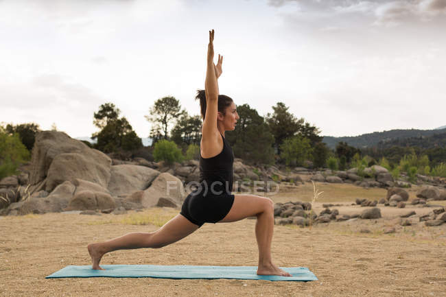 Mid adult woman in high lunge pose doing yoga outdoors on dam beach — Stock Photo