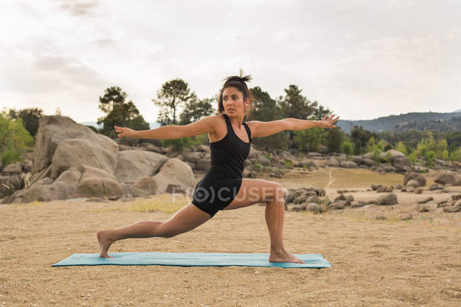 Mulher adulta média se alongando ao fazer ioga ao ar livre na praia da barragem — Fotografia de Stock