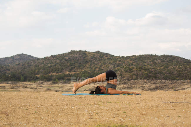 Mulher adulta média fazendo ioga ao ar livre na praia da barragem — Fotografia de Stock