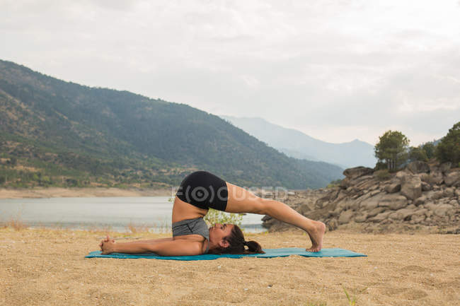 Mid adult woman doing yoga outdoors on dam beach — Stock Photo
