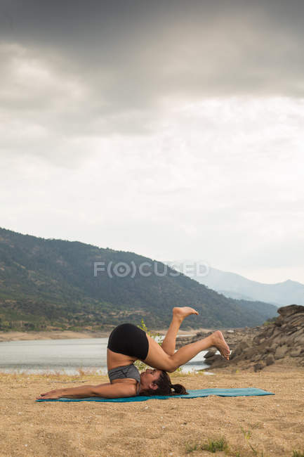 Mid adult woman with feet up doing yoga outdoors on dam beach — Stock Photo