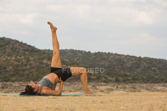 Mid adult woman with feet up doing yoga outdoors on dam beach — Stock Photo
