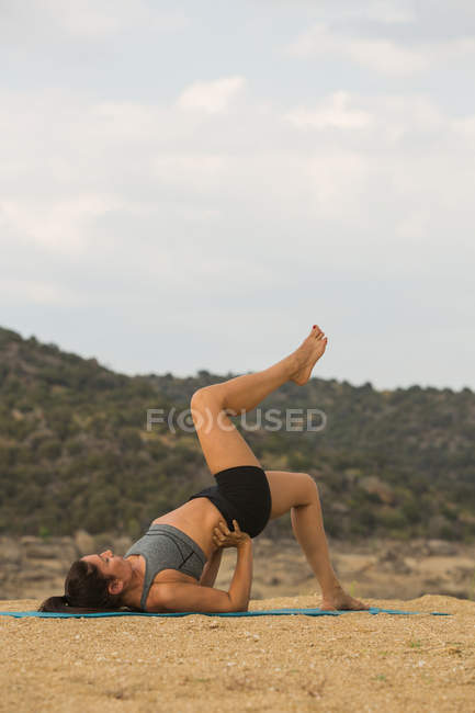 Femme adulte moyenne avec les pieds vers le haut faire du yoga en plein air sur la plage de barrage — Photo de stock
