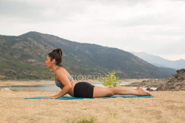 Mid adult woman in cobra pose doing yoga outdoors on dam beach — Stock Photo