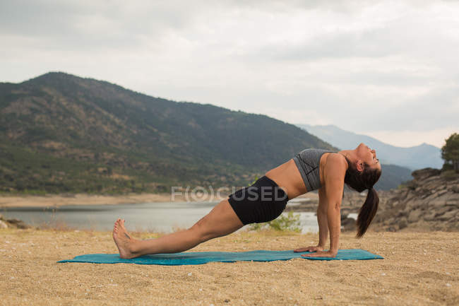 Femme adulte moyenne faisant du yoga à l'extérieur sur la plage du barrage — Photo de stock