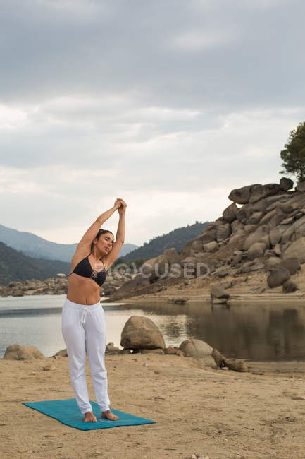 Femme adulte moyenne s'étirant tout en faisant du yoga à l'extérieur sur la plage du barrage — Photo de stock