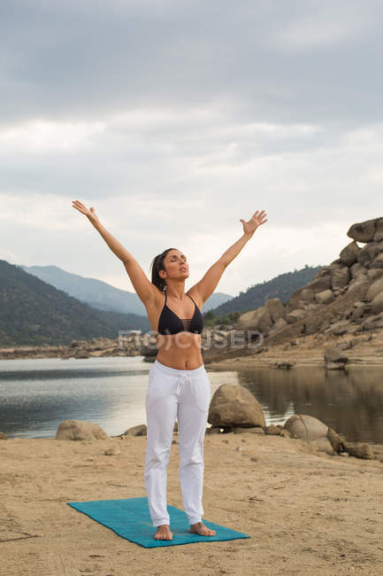 Взрослая женщина растягивается во время занятий йогой на открытом воздухе на дамбе пляжа — стоковое фото