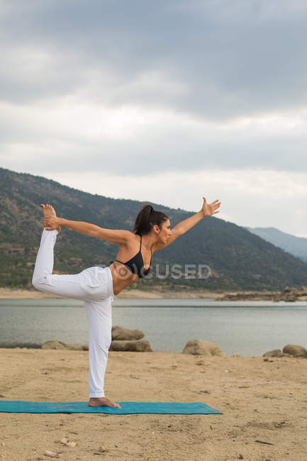 Femme adulte moyenne faisant du yoga à l'extérieur sur la plage du barrage — Photo de stock