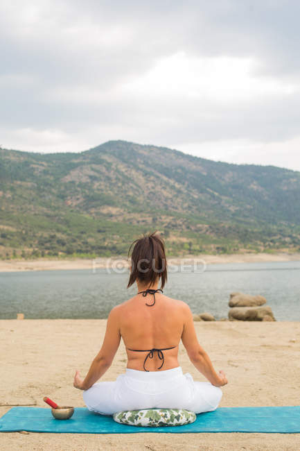 Задний вид медитирующей женщины в позе йоги лотоса на открытом воздухе на пляже дамбы — стоковое фото