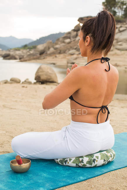 Mid adult woman meditating in lotus yoga pose outdoors on dam beach — Stock Photo