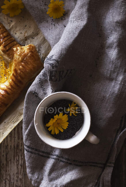 Becher aromatischer Kräutertee mit gelben Blüten auf Stoffserviette in der Nähe eines frischen Kuchenstücks — Stockfoto