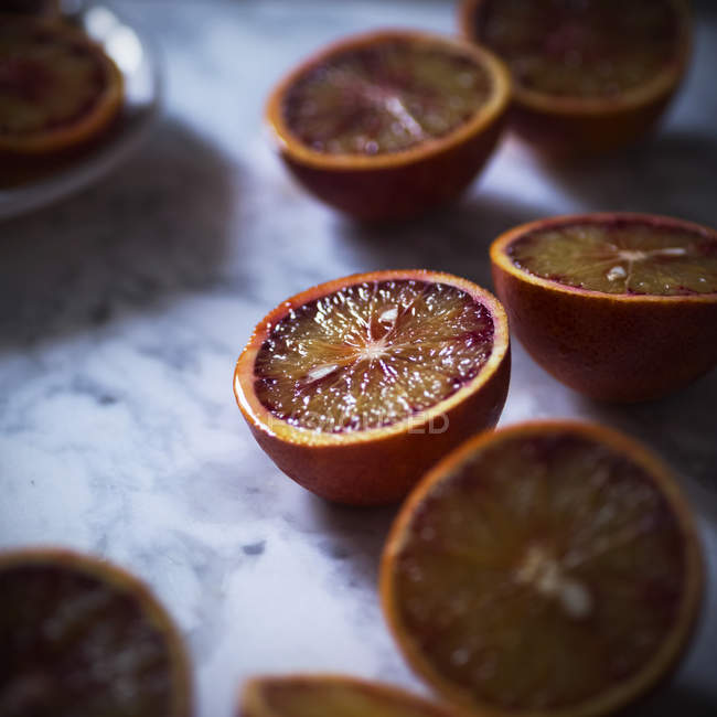 Primer plano de naranjas frescas a la mitad de la sangre en la mesa de mármol blanco - foto de stock