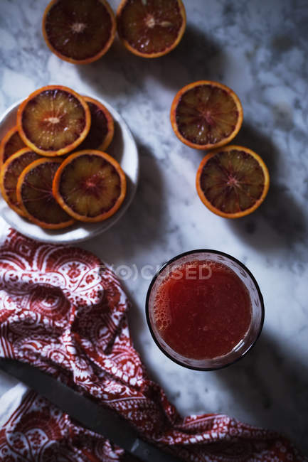 Glass of fresh juice and slices of blood orange on marble tabletop — Stock Photo