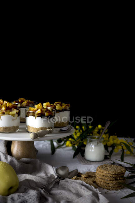 Verschiedene köstliche Desserts und Snacks auf dem Tisch neben Serviette und Blumen vor schwarzem Hintergrund platziert — Stockfoto