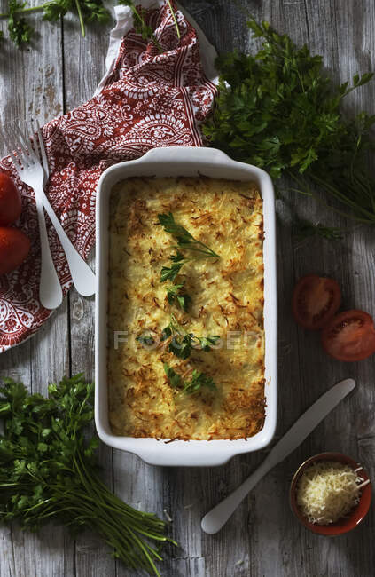 From above parsley and tomatoes placed on wooden tabletop around baking pan with palatable cheese dish — Stock Photo