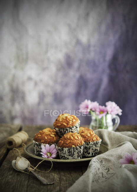 Plate with tasty grain muffins placed near linen napkin and pink flowers on wooden tabletop — Stock Photo
