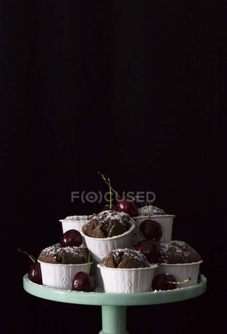 Chocolate cupcakes and fresh cherries on cake stand on black background — Stock Photo
