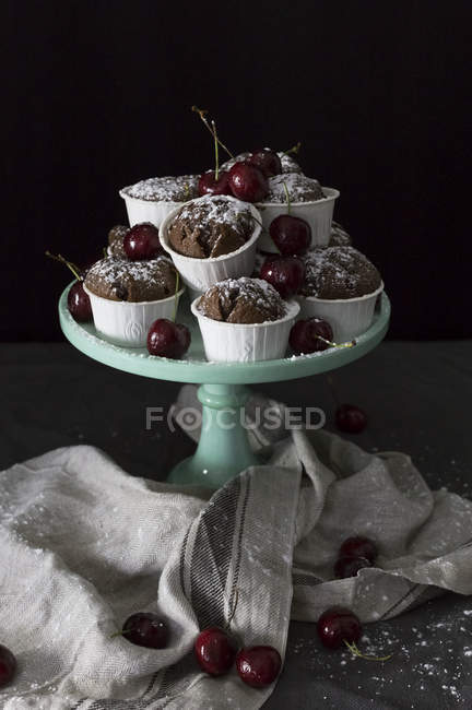 Chocolate cupcakes and fresh cherries on cake stand on black background — Stock Photo