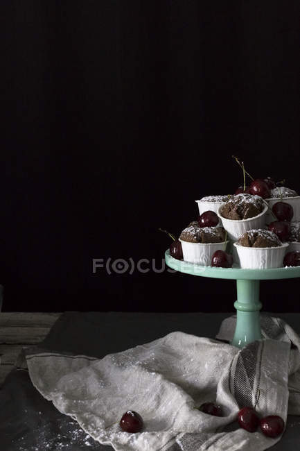 Cupcakes de chocolate y cerezas frescas en pie de pastel sobre fondo negro - foto de stock