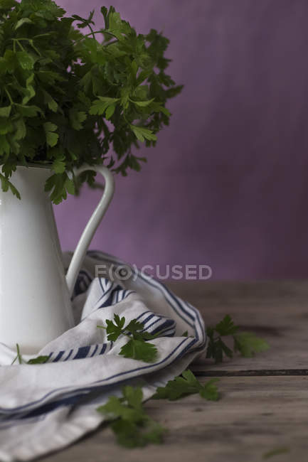 Primer plano de racimo de perejil fresco verde en jarra de cerámica sobre mesa de madera - foto de stock