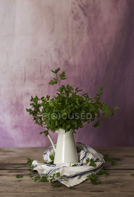 Manojo de perejil verde fresco en jarra de cerámica sobre mesa de madera - foto de stock