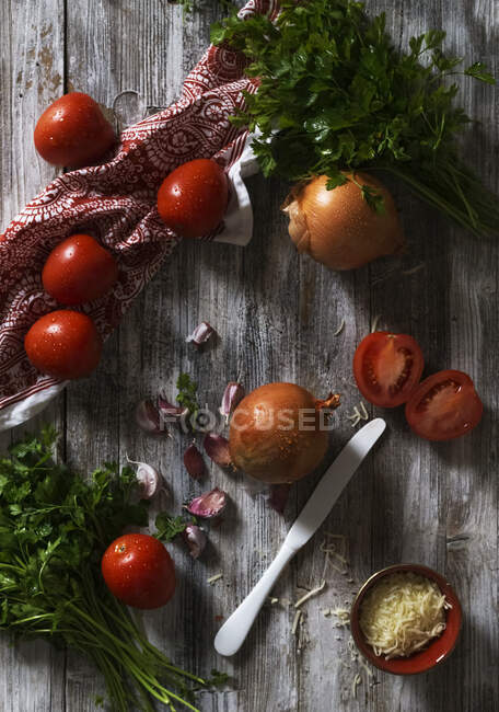 From above Fresh ripe tomatoes and onions with garlic and parsley placed on shabby wooden tabletop near napkin — Stock Photo