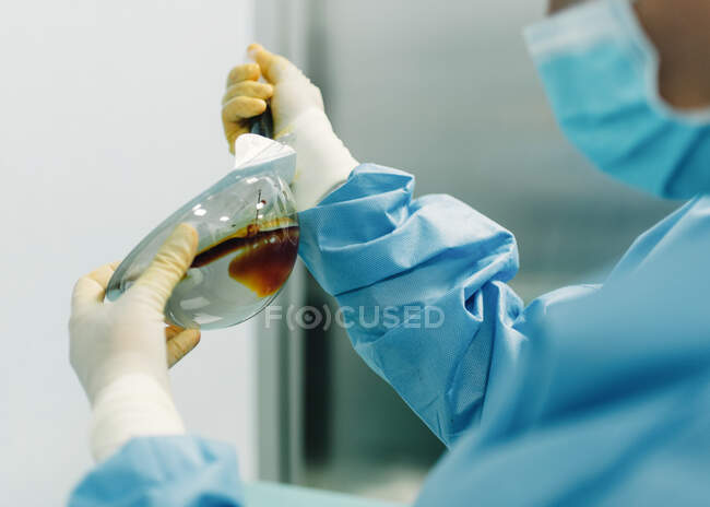Погляд на медика в хірургічній сукні, що впорскує йоду в пластикову коробку з імплантатом для дезінфекції під час операції. — Stock Photo