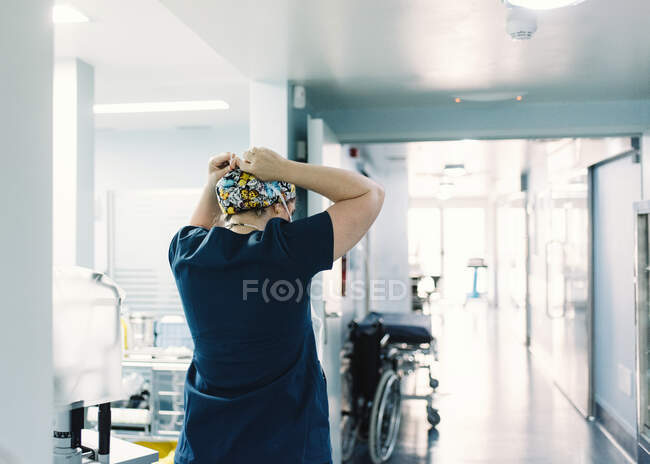Vista posterior del médico en uniforme de hospital azul de pie y preparándose para la cirugía en el pasillo de la clínica - foto de stock