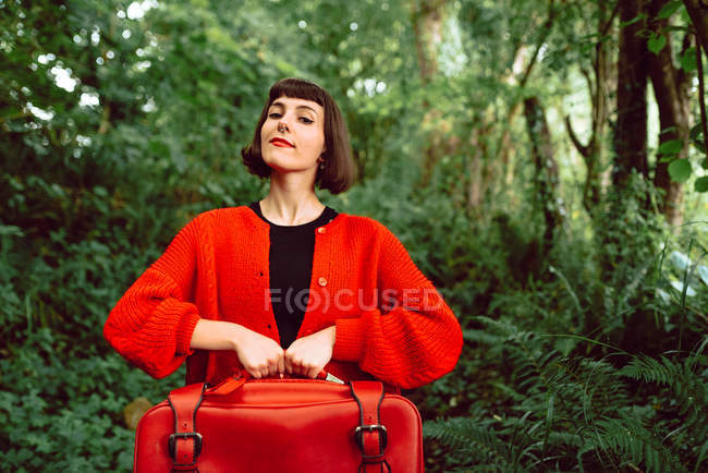 Donna in rosso con grande valigia rossa nella foresta — Foto stock