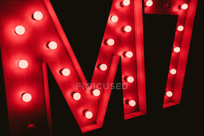 Enorme letra M con bombillas brillantes de neón rojo en la pared negra en la oscuridad - foto de stock
