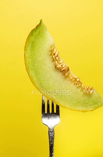 Tasty juicy slice of pitted melon served on fork on yellow background — Stock Photo