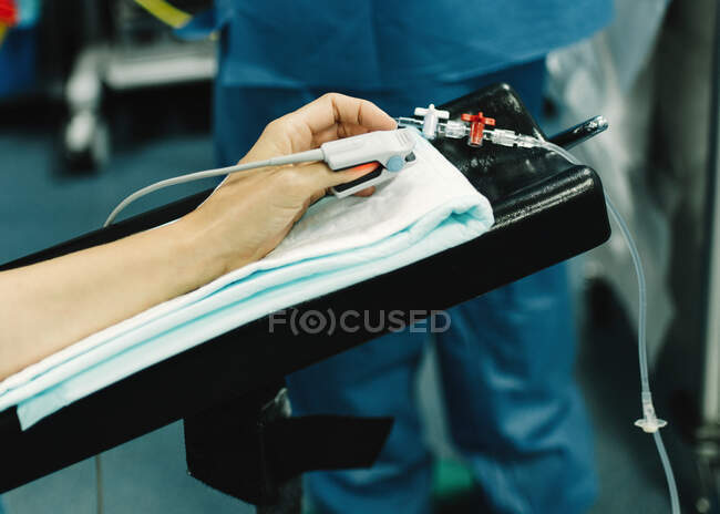 From above crop hand with clip sensor on finger and catheter before surgery and nurse standing beside — Stock Photo