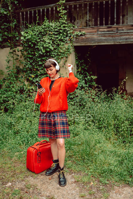Жінка в навушниках з валізою слухає музику в сільській місцевості — стокове фото