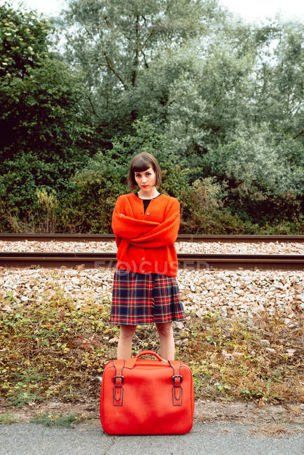 Mulher de vermelho com mala vintage em pé na estação de trem no campo — Fotografia de Stock