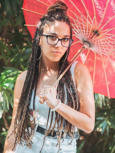 Струнка молода жінка в літньому вбранні з парасолькою, що стоїть в саду — стокове фото