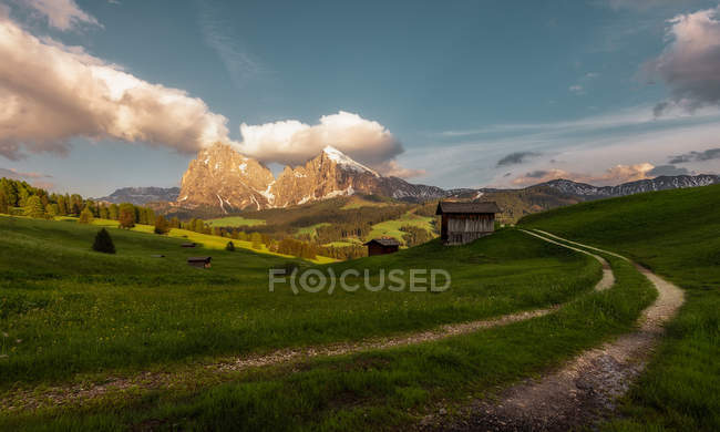 Узкая тропа к маленькому домику на зеленой долине с горами на заднем плане в Доломитовых Альпах, Италия — стоковое фото