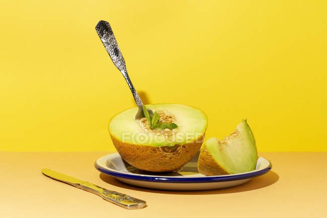 Cut ripe appetizing sweet pitted melon on plate with spoon and fork on yellow background — Stock Photo