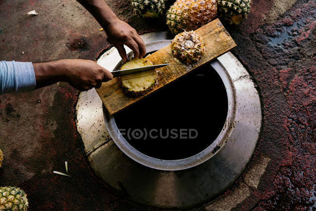 Зверху людина рубає ананас з ножем на металевому резервуарі в денне світло — стокове фото