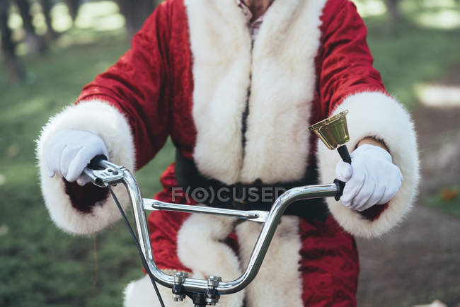 Неузнаваемый человек в костюме Санта-Клауса сидит на велосипеде и звонит в колокол — стоковое фото