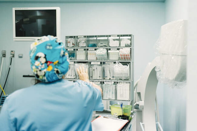 Visão traseira do médico feminino de uniforme azul levando suprimentos necessários para a cirurgia no hospital — Fotografia de Stock