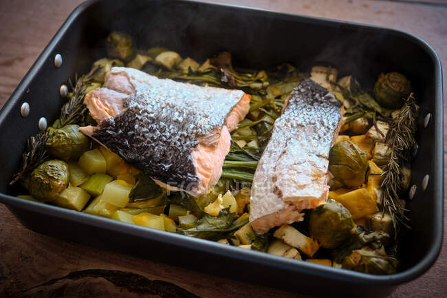 Сверху обжига кастрюля с большими кусками лосося с кожей на гарнире из разнообразных выпеченных овощей и зелени — стоковое фото