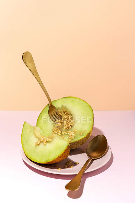 Cut ripe sweet melon on plate with spoon and fork on pink table — Stock Photo